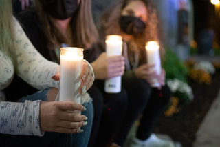 Members of @standwithsurvivorssu sit together holding candles, listening to the speakers.